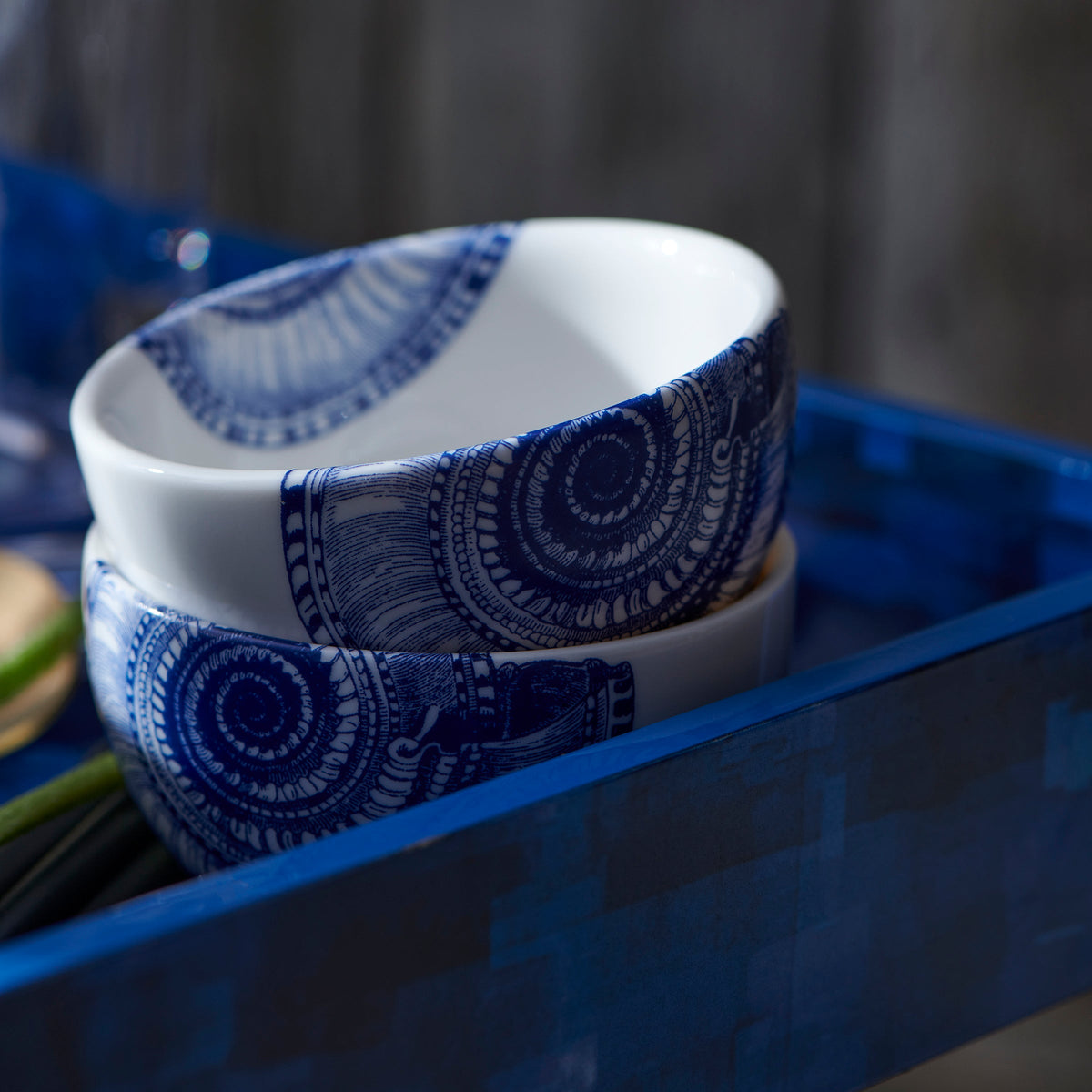 A small, blue and white Shells Snack Bowl resembling a nautilus shell treasure on a tray by Caskata Artisanal Home.
