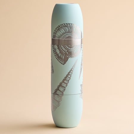 A Caskata x High Camp light blue cylindrical insulated wine flask featuring silver seashell illustrations on a beige background.