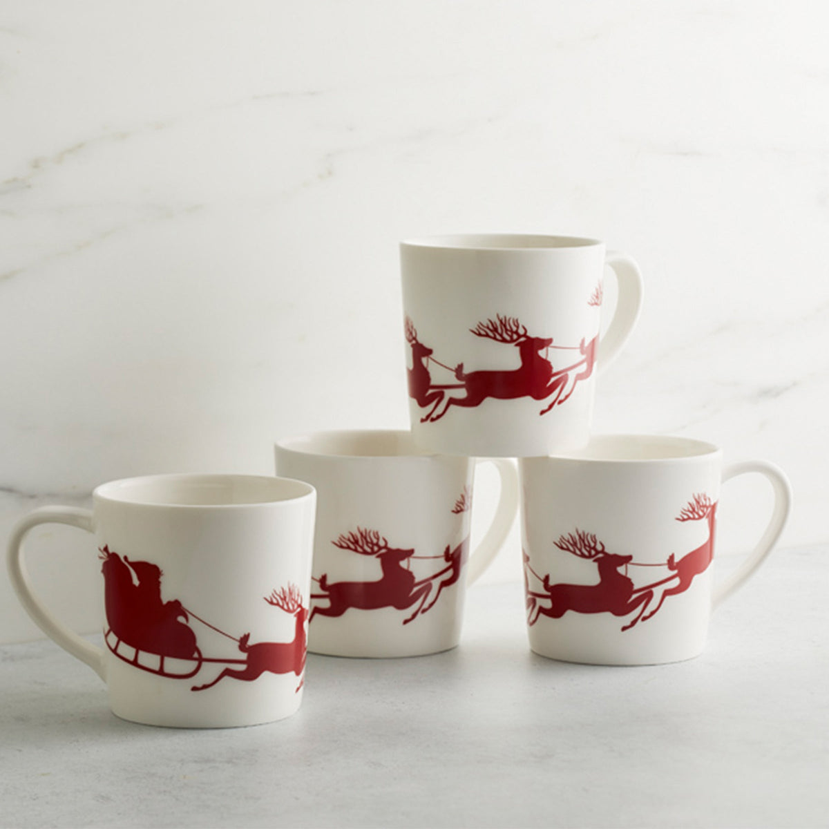 Four holiday-themed Sleigh Mugs with red reindeer on them from Caskata Artisanal Home.