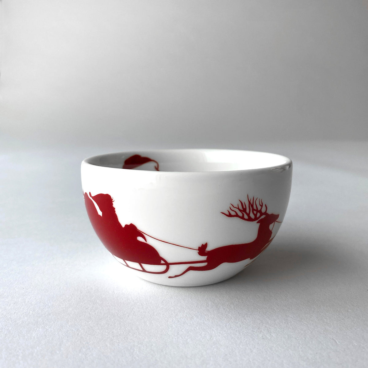 A Sleigh Snack Bowl by Caskata Artisanal Home, featuring Santa Claus and his reindeer, perfect for serving appetizers and spreading holiday spirits.