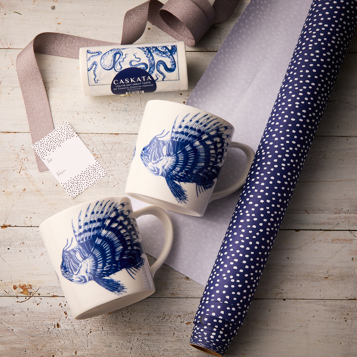 The "Spiky Fish Coffee Talk" Bundle by Caskata includes two white porcelain mugs with blue fish, a bar of soap, ribbon, gift tag, and blue polka dot wrapping paper—perfect for any marine lover.