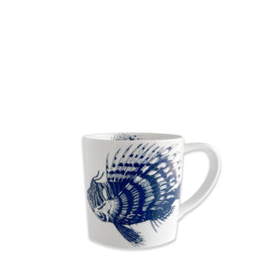 The Caskata Spiky Fish Mug features a white ceramic design with a detailed blue fish illustration and handle on the right, making it ideal for adding coastal charm to your tableware collection.
