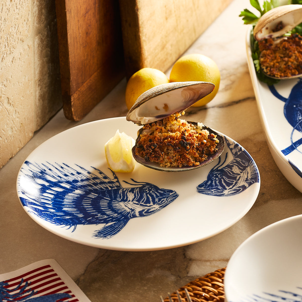 The Caskata Spiky Fish Coupe Salad Plate is a white porcelain plate with two detailed blue fish, perfect for adding coastal charm to your dinnerware.
