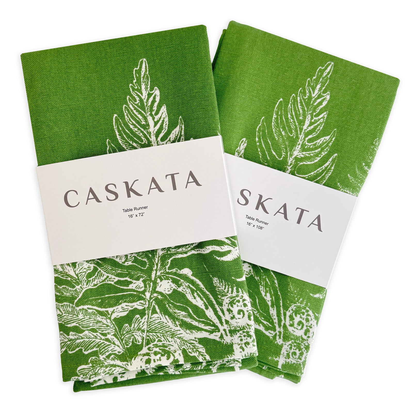Two Spring Verde Table Runners by Caskata—green cotton runners with white fern designs, each folded and wrapped with a branded label—perfect for cottage-core table decor.