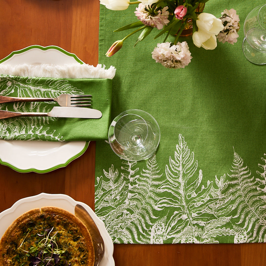 Two Spring Verde Table Runners by Caskata—green cotton runners with white fern designs, each folded and wrapped with a branded label—perfect for cottage-core table decor.