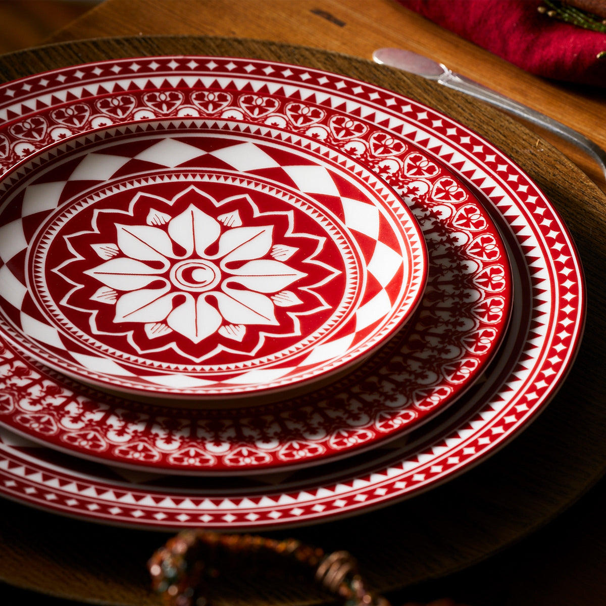 A Fez Crimson Rimmed Dinner Plate from Caskata Artisanal Home on a rustic table.