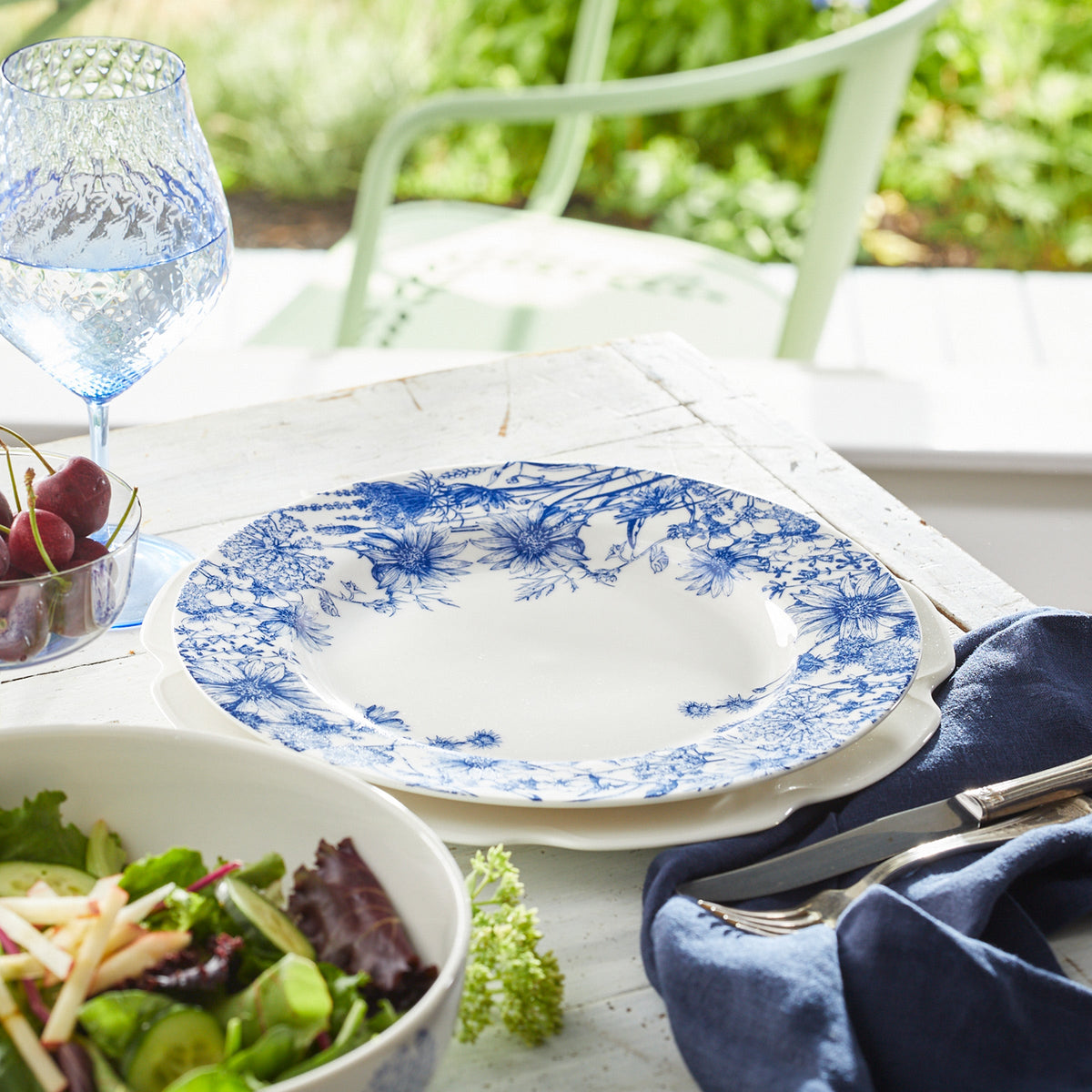 A Summer Blues Rimmed Dinner Plate by Caskata Artisanal Home with a floral pattern on a white table.
