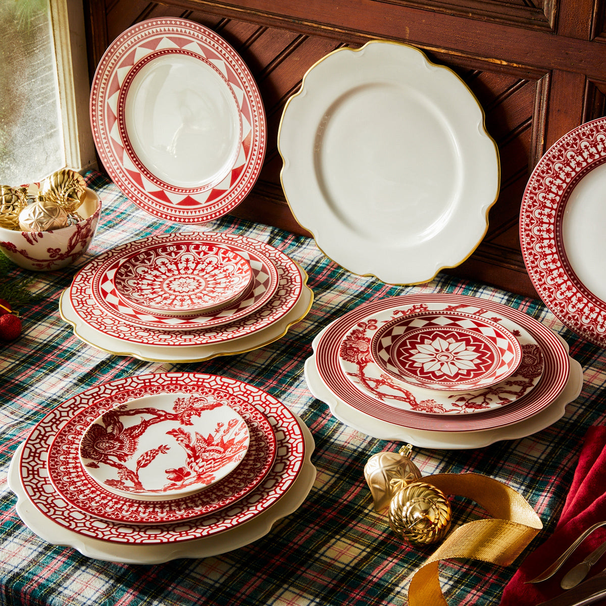 Gracefully placed on a table, a set of Caskata Artisanal Home&#39;s Grace Gold Dinner Plates adorned with vibrant red curves creates an elegant display.