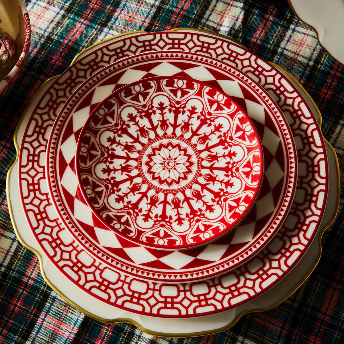 A red and white Grace Gold Dinner Plate by Caskata Artisanal Home on a polished table.