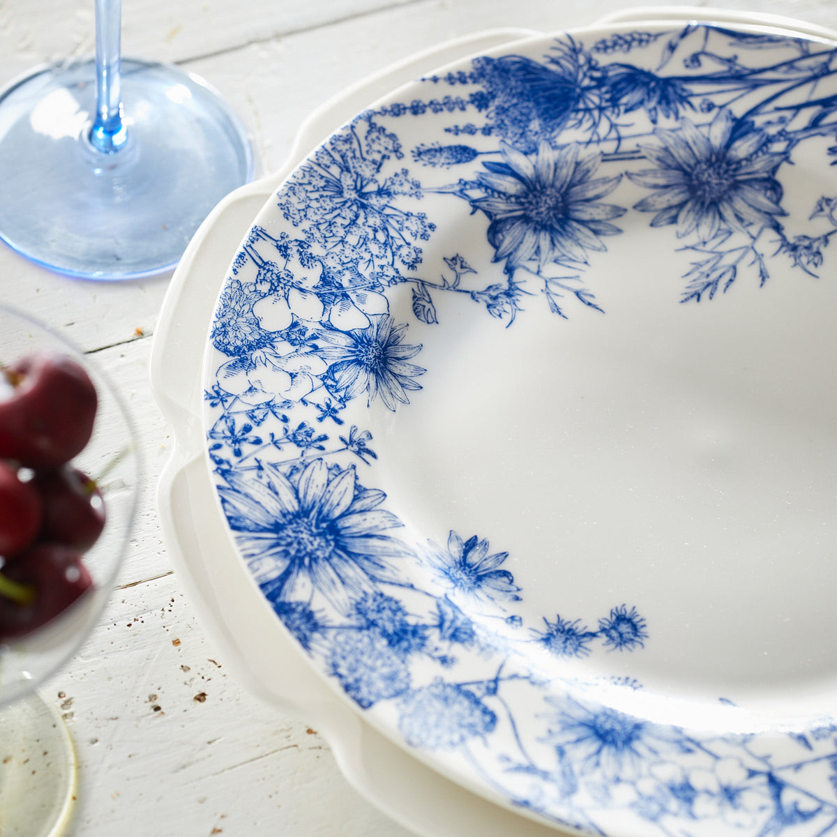 A Summer Blues Rimmed Dinner Plate by Caskata Artisanal Home with a glass of wine.