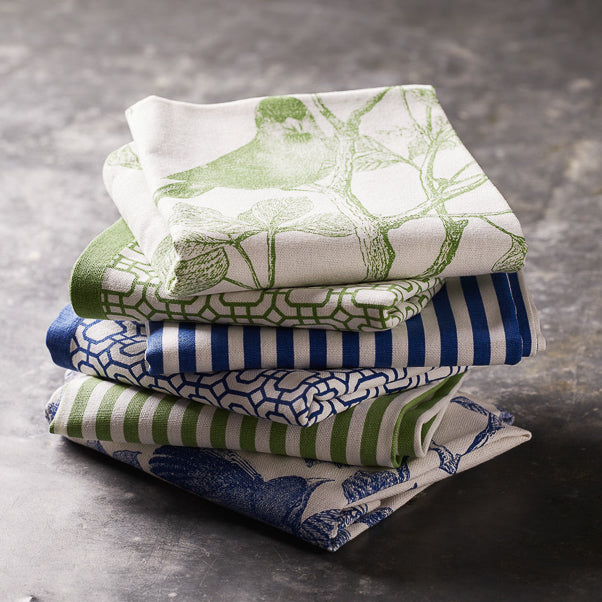 A stack of Newport Garden Gate Dinner Napkins in Green Set/4 from Caskata with birds on them.