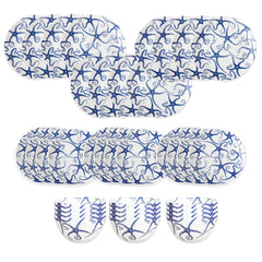 The Caskata Starfish Table for 12 set features oval and round white plates plus three bowls, all adorned with intricate blue swirled patterns like blue and white porcelain, arranged in rows on a white background.