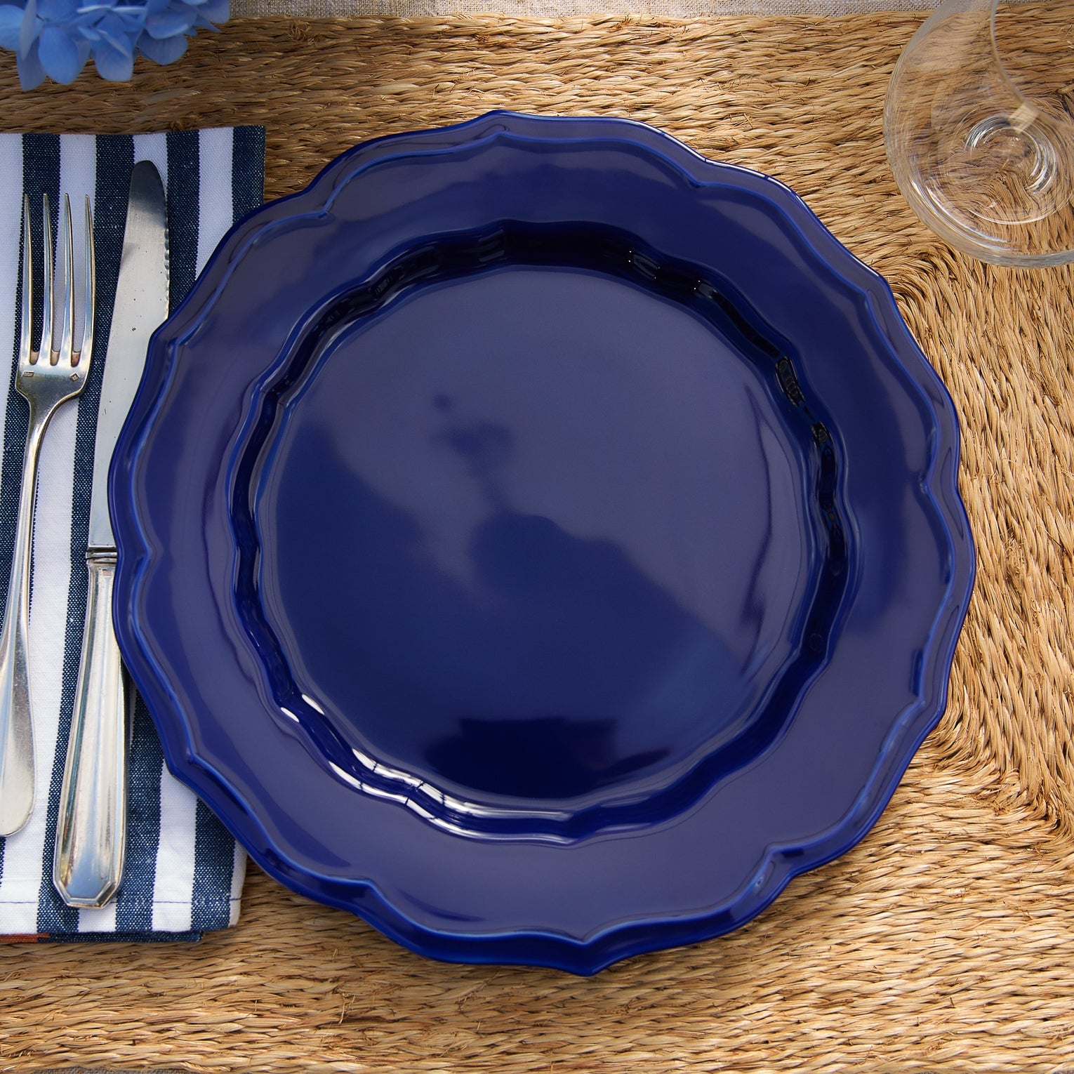 A round, dark blue Caskata Stella Scalloped Solid Blue Dinner Plate with a scalloped edge.