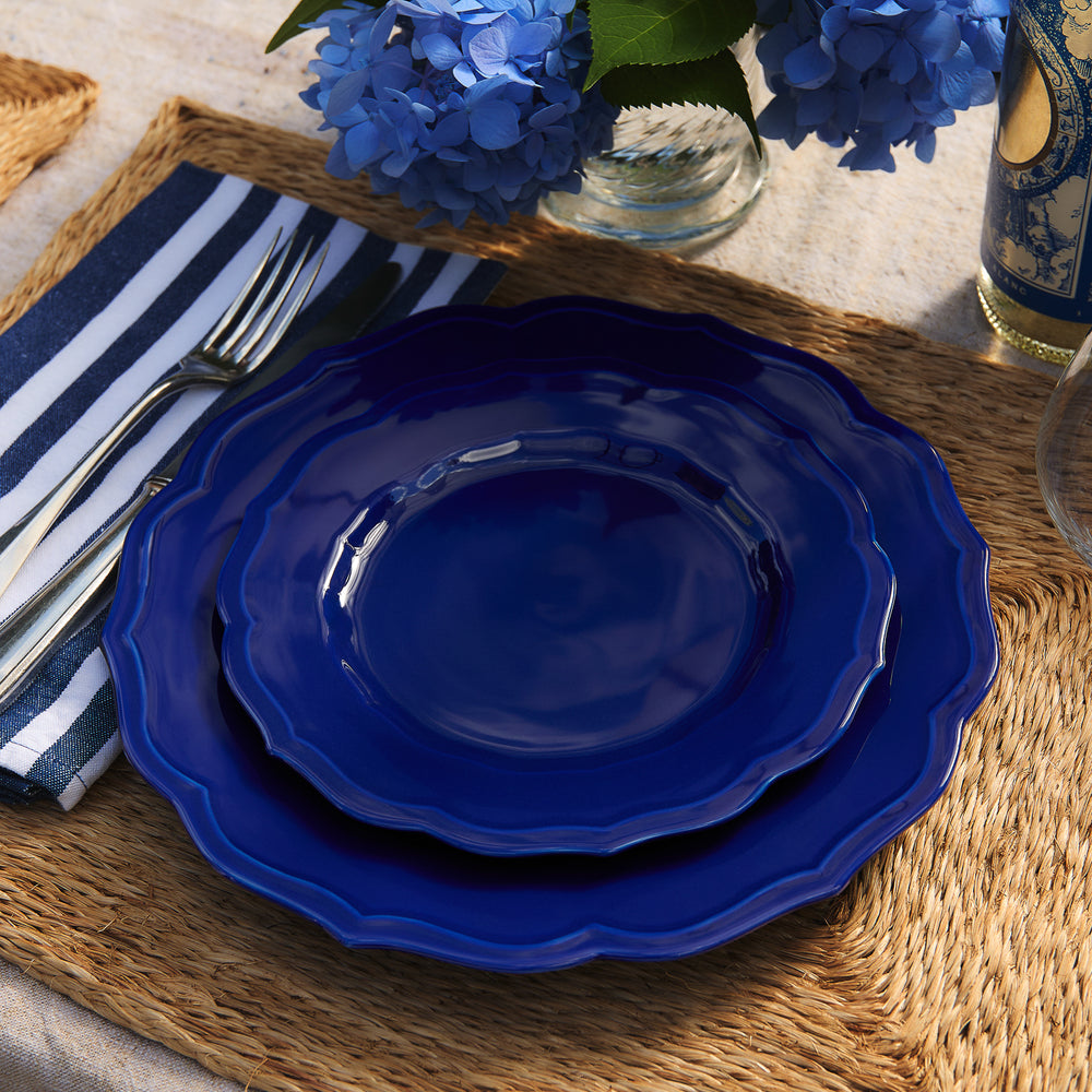 Two Stella Scalloped Solid Blue Salad Plates stacked on a woven placemat with a striped napkin and silverware.