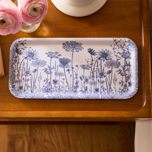 A Caskata Summer Blues Small Rectangular Birchwood Tray, featuring blue floral patterns on white, sits on wood with pink flowers nearby, highlighting its eco-friendly design.