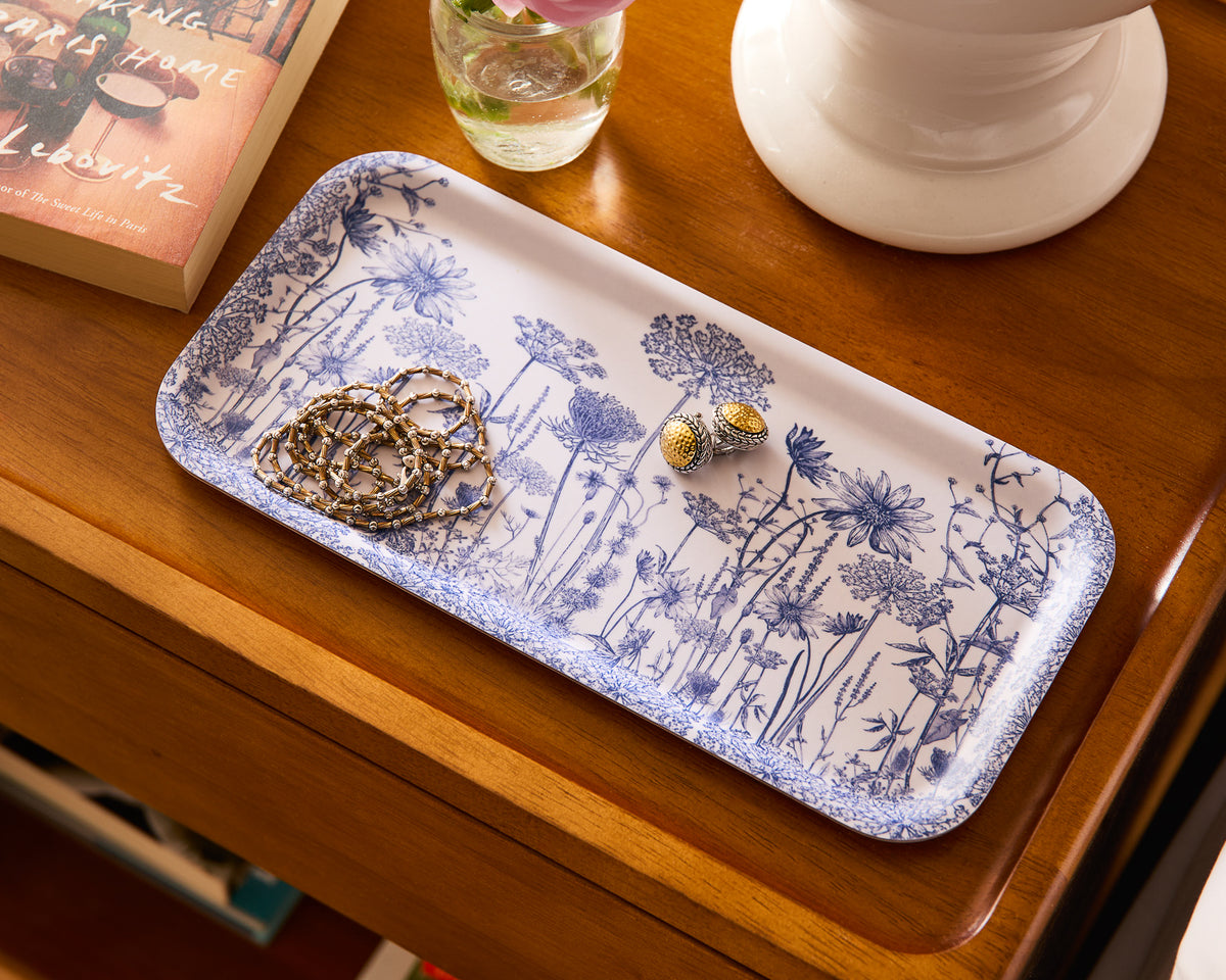 Caskata's Summer Blues Small Rectangular Birchwood Tray elegantly displays earrings and a chain necklace. Accompanied by a book and a white vase with pink flowers, it adds an effortlessly chic, sustainable touch to any space.