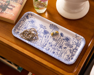 Caskata's Summer Blues Small Rectangular Birchwood Tray elegantly displays earrings and a chain necklace. Accompanied by a book and a white vase with pink flowers, it adds an effortlessly chic, sustainable touch to any space.