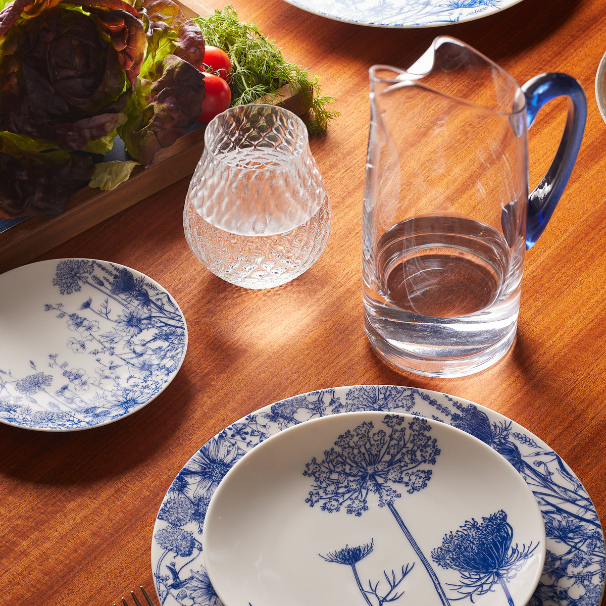 A Summer Blues Coupe Salad Plate from Caskata Artisanal Home, a blue and white plate on a wooden table.