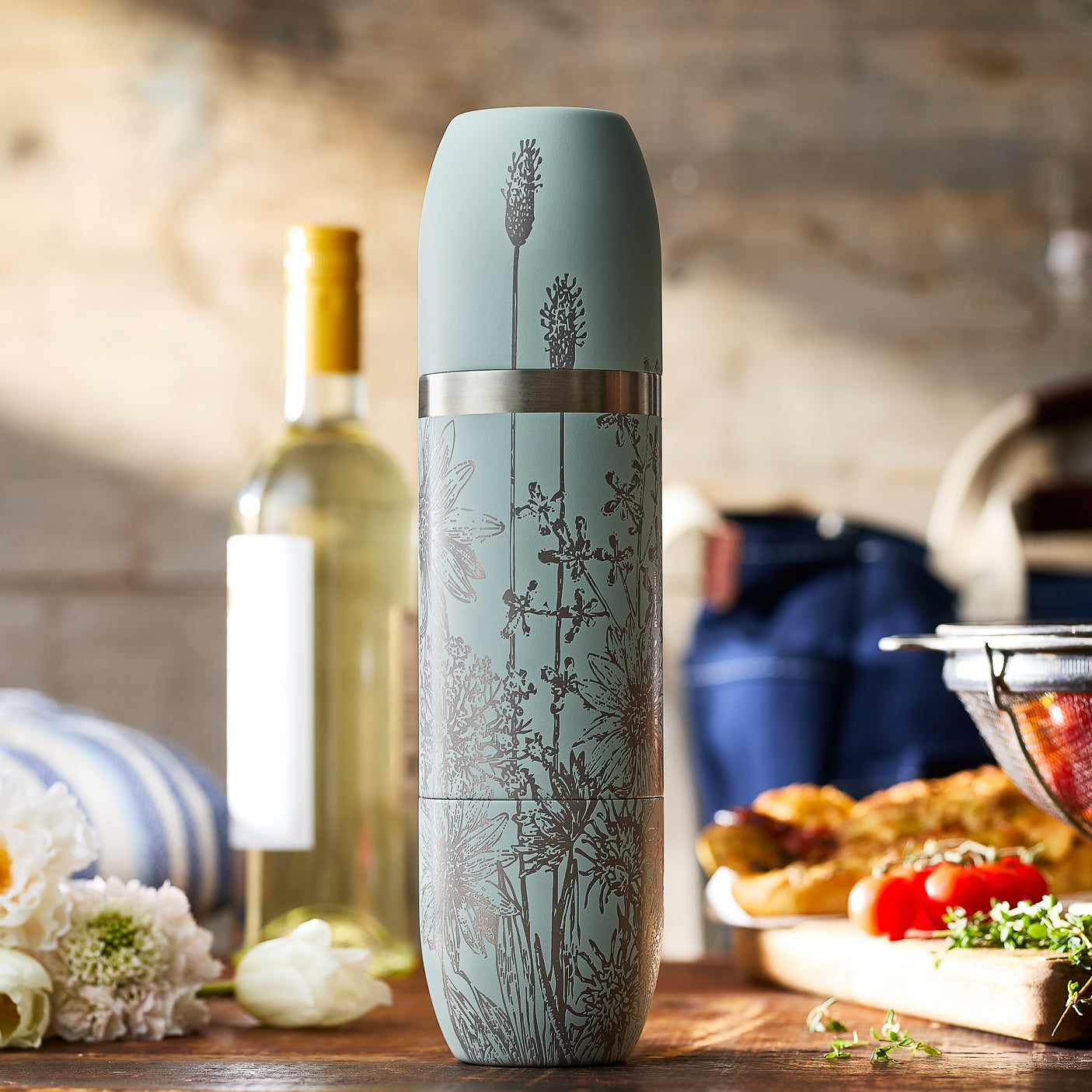 The Caskata x High Camp Light Blue Summer Parkside Flask, by Caskata, features a floral design and comes with matching packaging—perfect for outdoor adventures and summer gatherings.