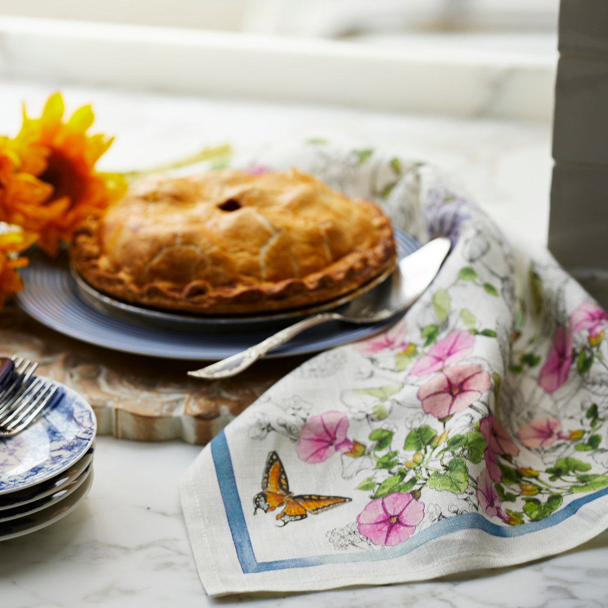 An exquisite pie is elegantly presented on a table adorned with beautiful flowers, surrounded by TTT Nasturtium Linen Kitchen Towels Set/2 for added charm.