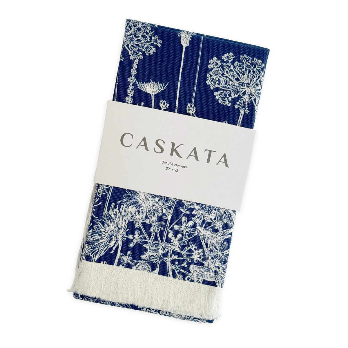 The Caskata Summer Blues Dinner Napkins feature a navy blue base with white botanical prints and a white fringe, neatly folded to add cottage-core charm to your table linens.