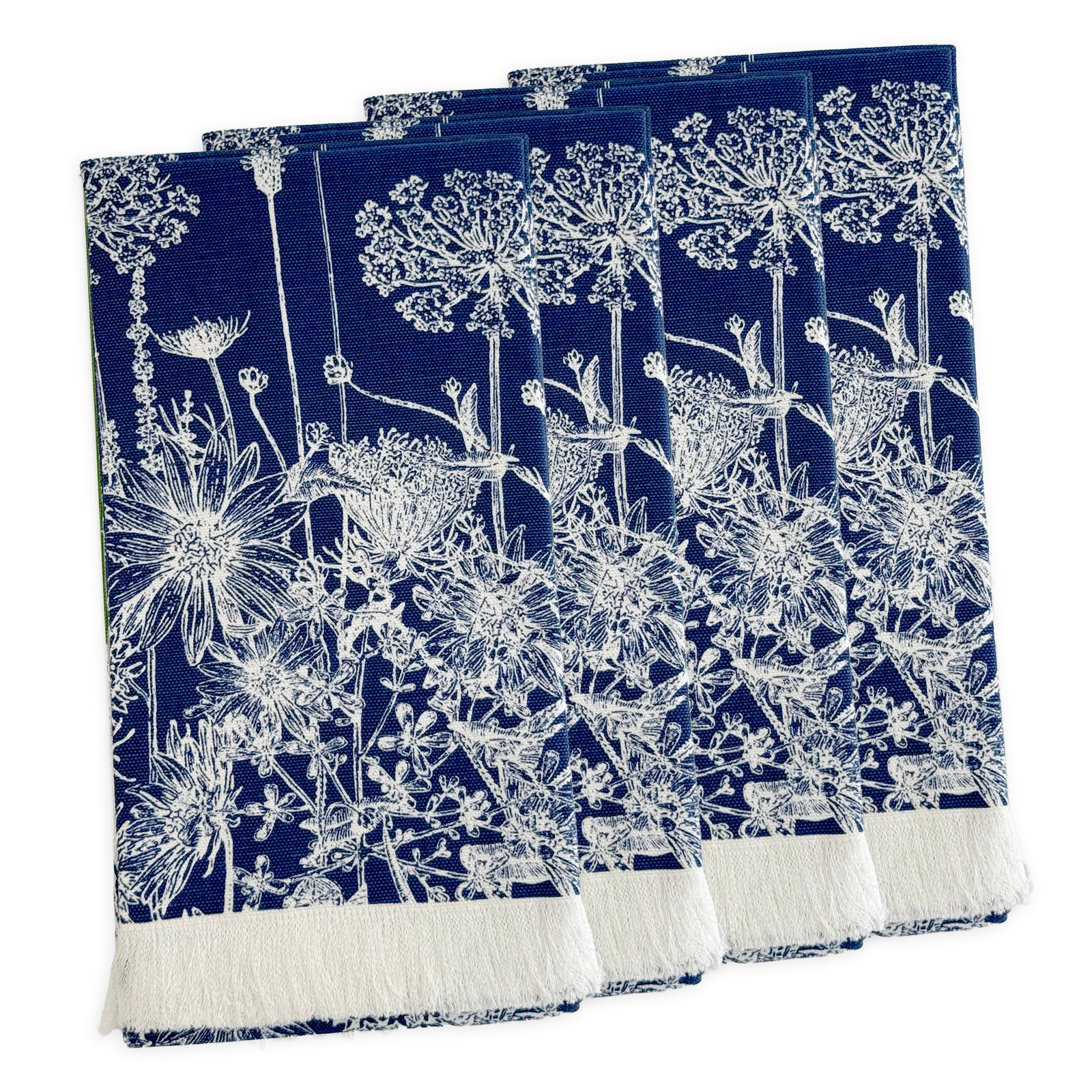 A set of four Summer Blues Dinner Napkins by Caskata in navy blue cotton with white floral patterns, inspired by New England wildflowers and finished with a white fringe on one edge, arranged in a slightly overlapping stack.