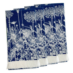 A set of four Summer Blues Dinner Napkins by Caskata in navy blue cotton with white floral patterns, inspired by New England wildflowers and finished with a white fringe on one edge, arranged in a slightly overlapping stack.