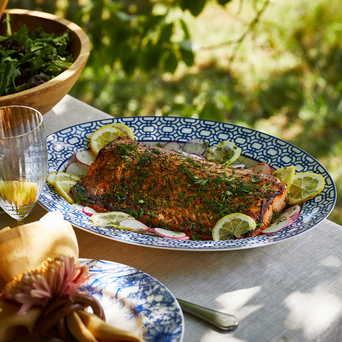 A plate of salmon with lemons and herbs on a Caskata Artisanal Home Newport Garden Gate Oval Rimmed Platter.
