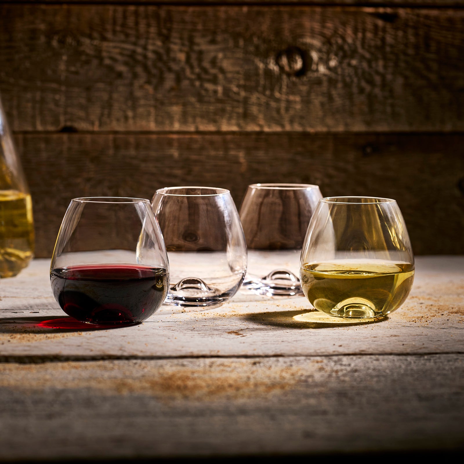 Four Tuesday Stemless Wine Glasses by Caskata are shown in a row; the left glass holds a dark liquid while the other three are empty. This set of four lead-free crystal tumblers suits any occasion.