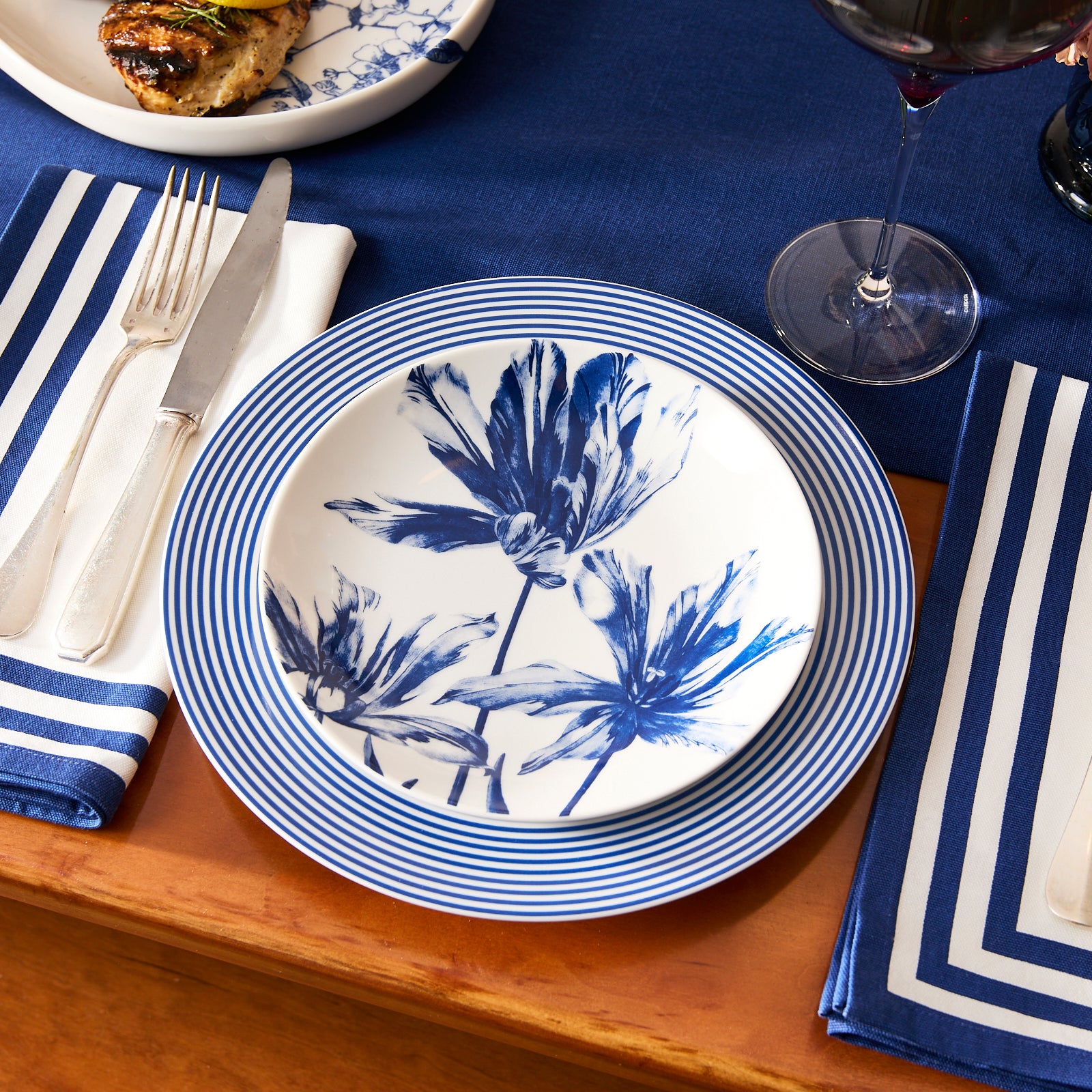 The Caskata Tulip Coupe Salad Plate features an elegant blue floral design with three stylized tulips and stems, beautifully displayed from above on a plain white background.
