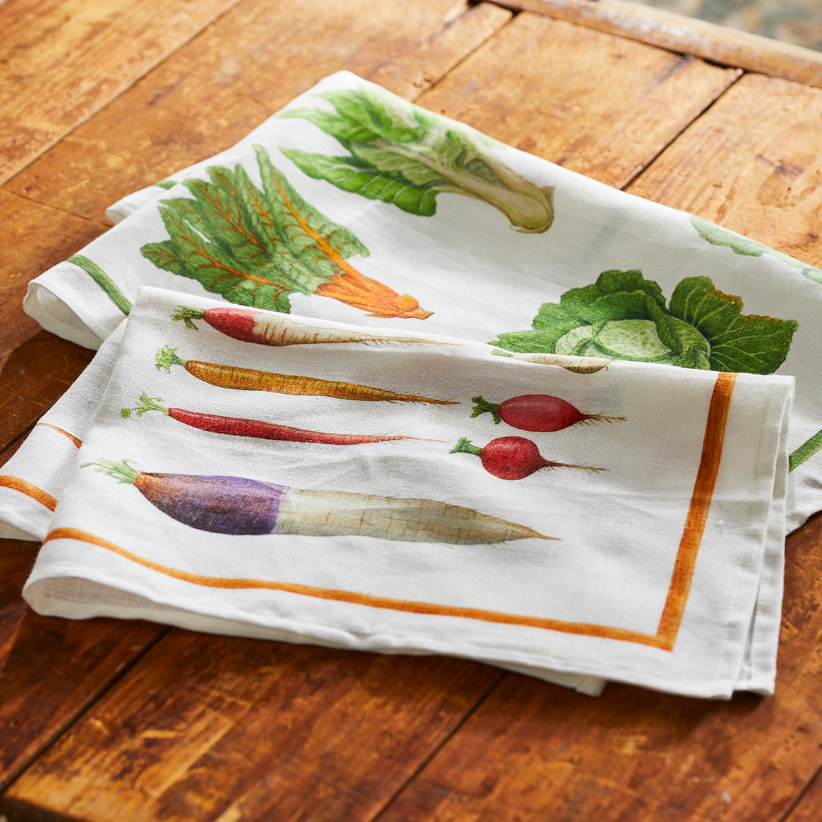 Two Veggies Linen Kitchen Towels with fresh veggies on them on a wooden table. (Brand: TTT)