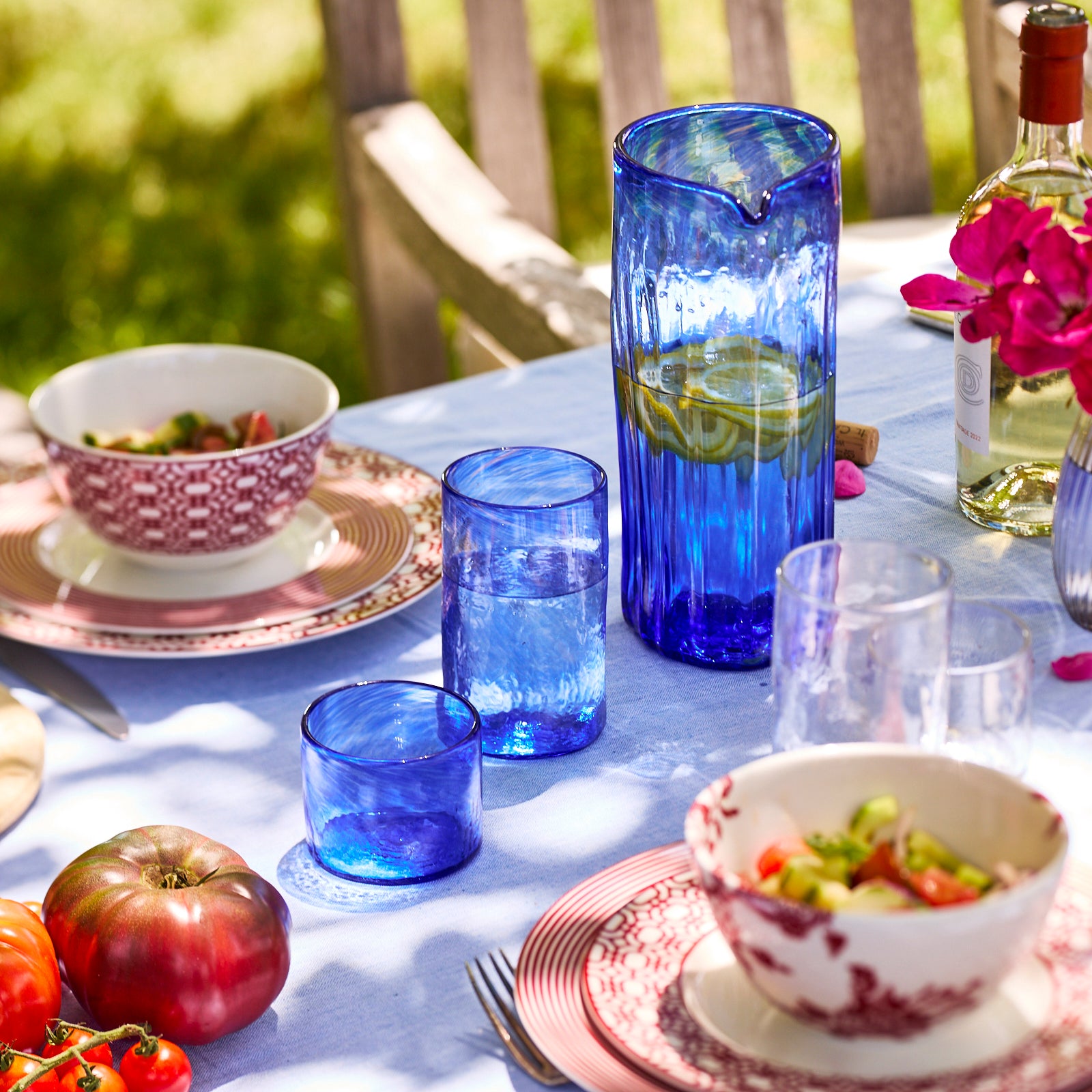 The Caskata Viento Large Cobalt Pitcher is a tall, handblown piece made from recycled glass. It features a transparent blue body with a long, clear handle and is displayed on a white background.