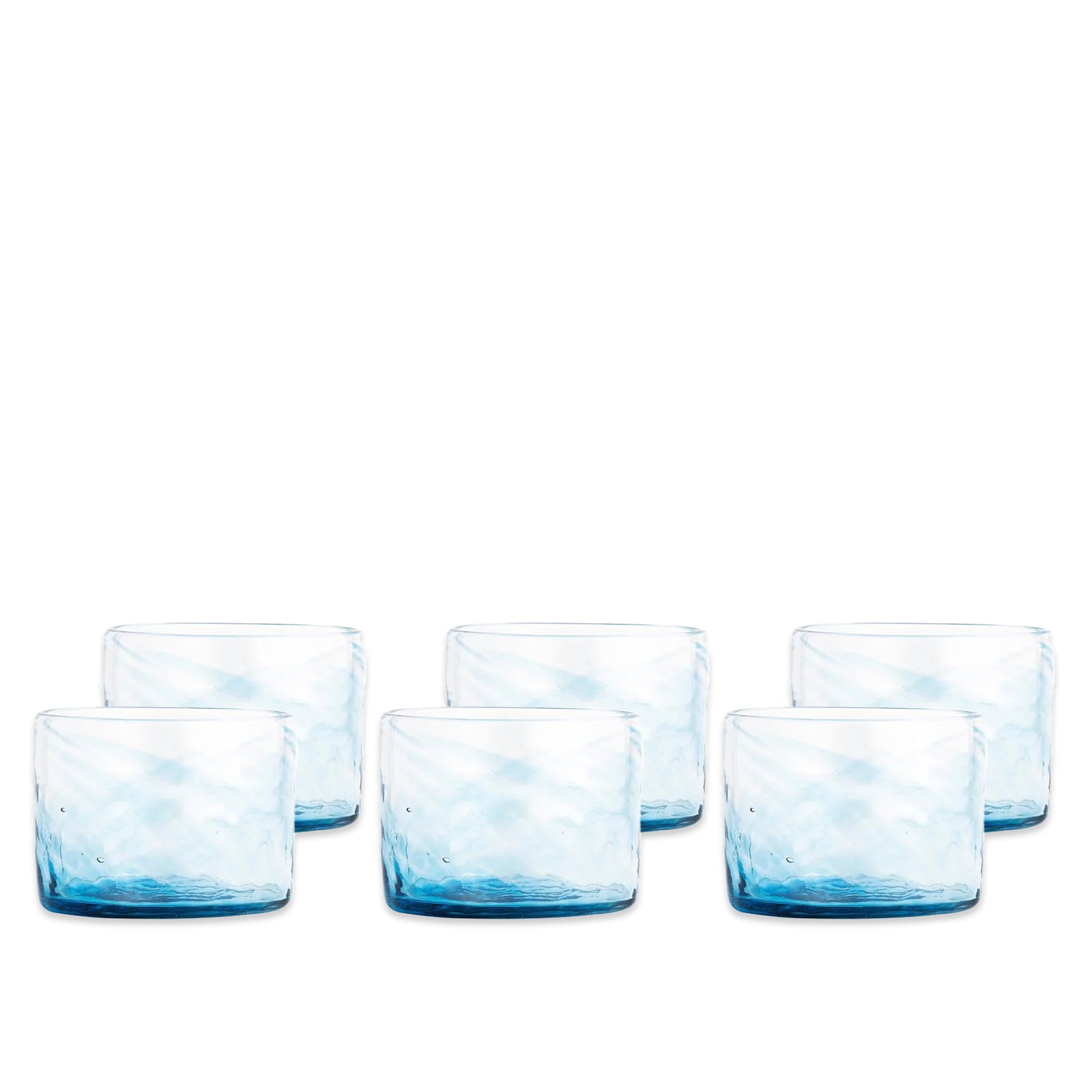 The Caskata Viento Small Blue Tumblers set includes six handblown glasses, each with a unique charm from subtly tinted recycled glass, arranged in two rows against a white background.