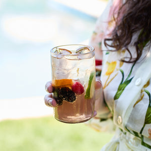 A person holds an iced drink with lime, orange, blackberry, and cherry in a Caskata Viento Large Clear Tumbler, set of 6.