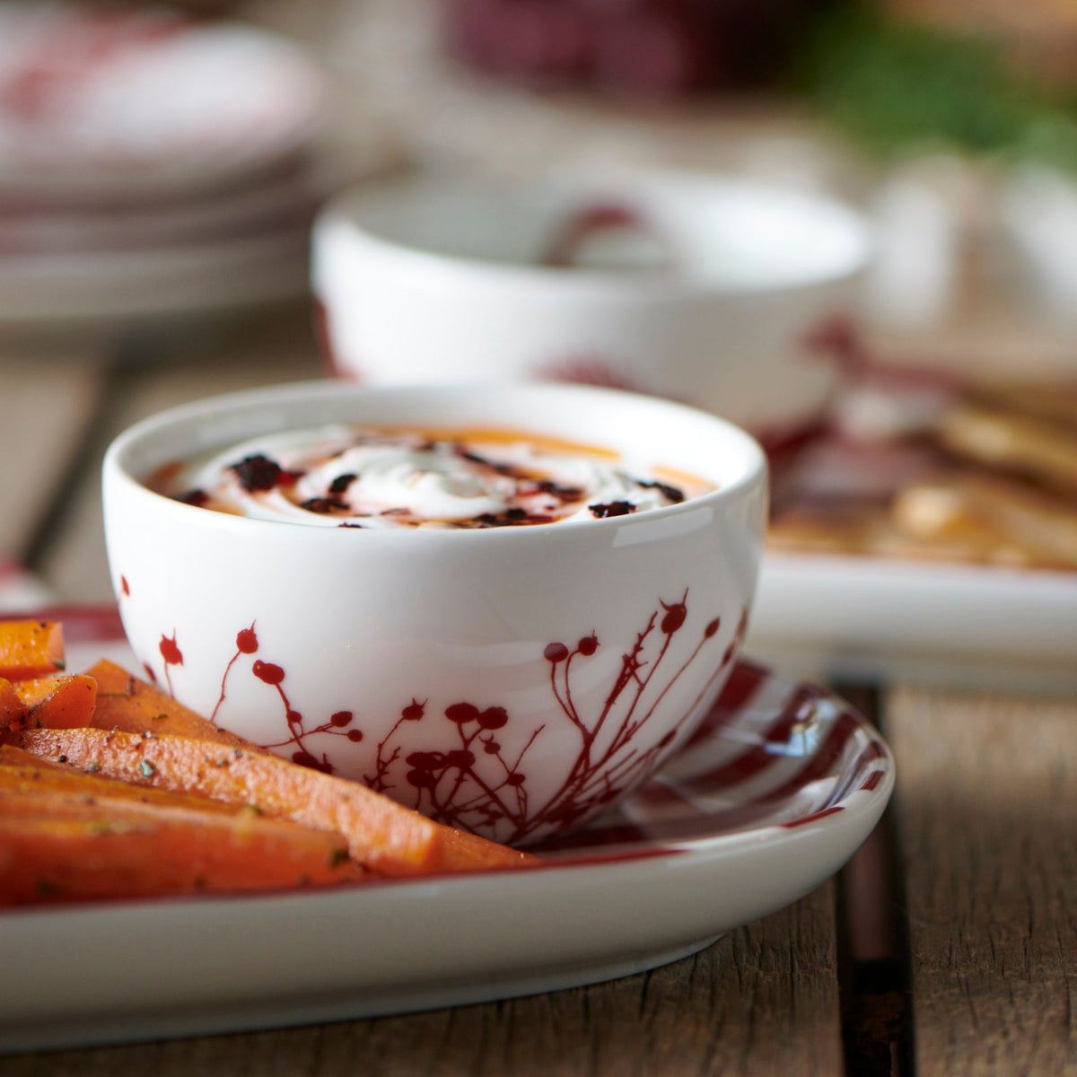 A Winterberries Snack Bowl with a plate of dip and a plate of carrots adorned with festive red berries, from Caskata Artisanal Home.