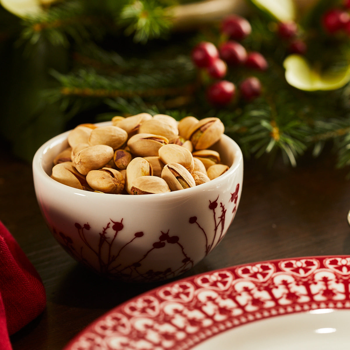 A bowl of pistachios and a plate on a table adorned with Caskata&#39;s Holiday Party V.1 Mixed Set of 12.