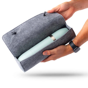 Two hands hold a grey Caskata Wool Parkside Flask Case containing a light blue cylindrical object against a white background.