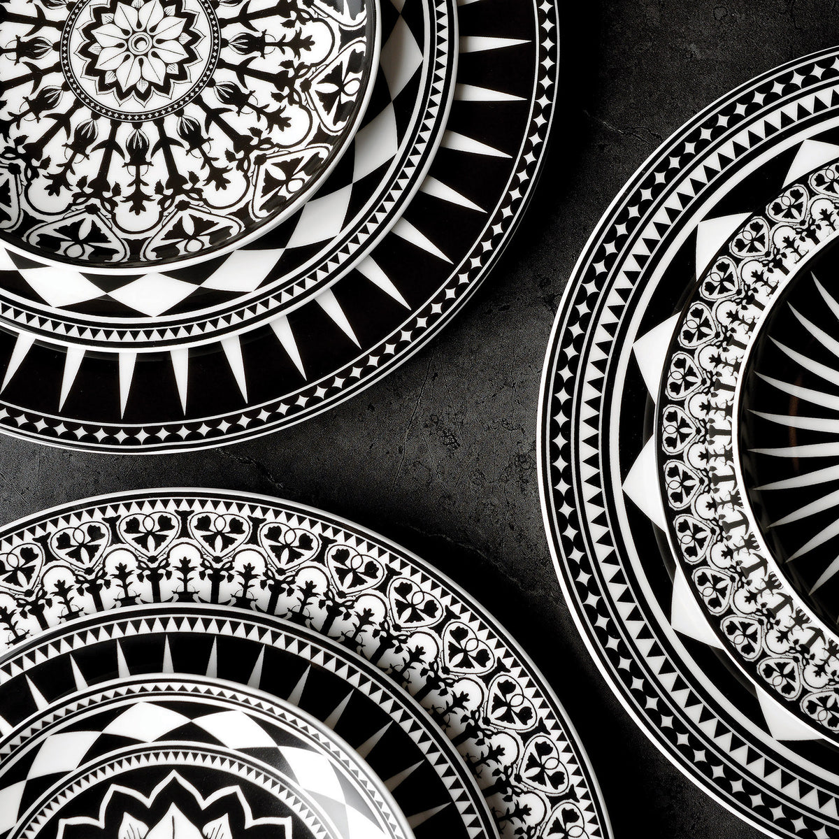 Black and white Casablanca Small Plates by Caskata Artisanal Home, with intricate geometric and floral patterns, arranged on a dark surface, showcasing heirloom-quality dinnerware.
