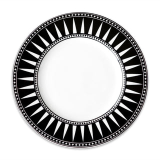 A round white plate with a black rim features a sophisticated geometric pattern of triangles and lines in white, reminiscent of the Marrakech Rimmed Dinner Plate by Caskata Artisanal Home.