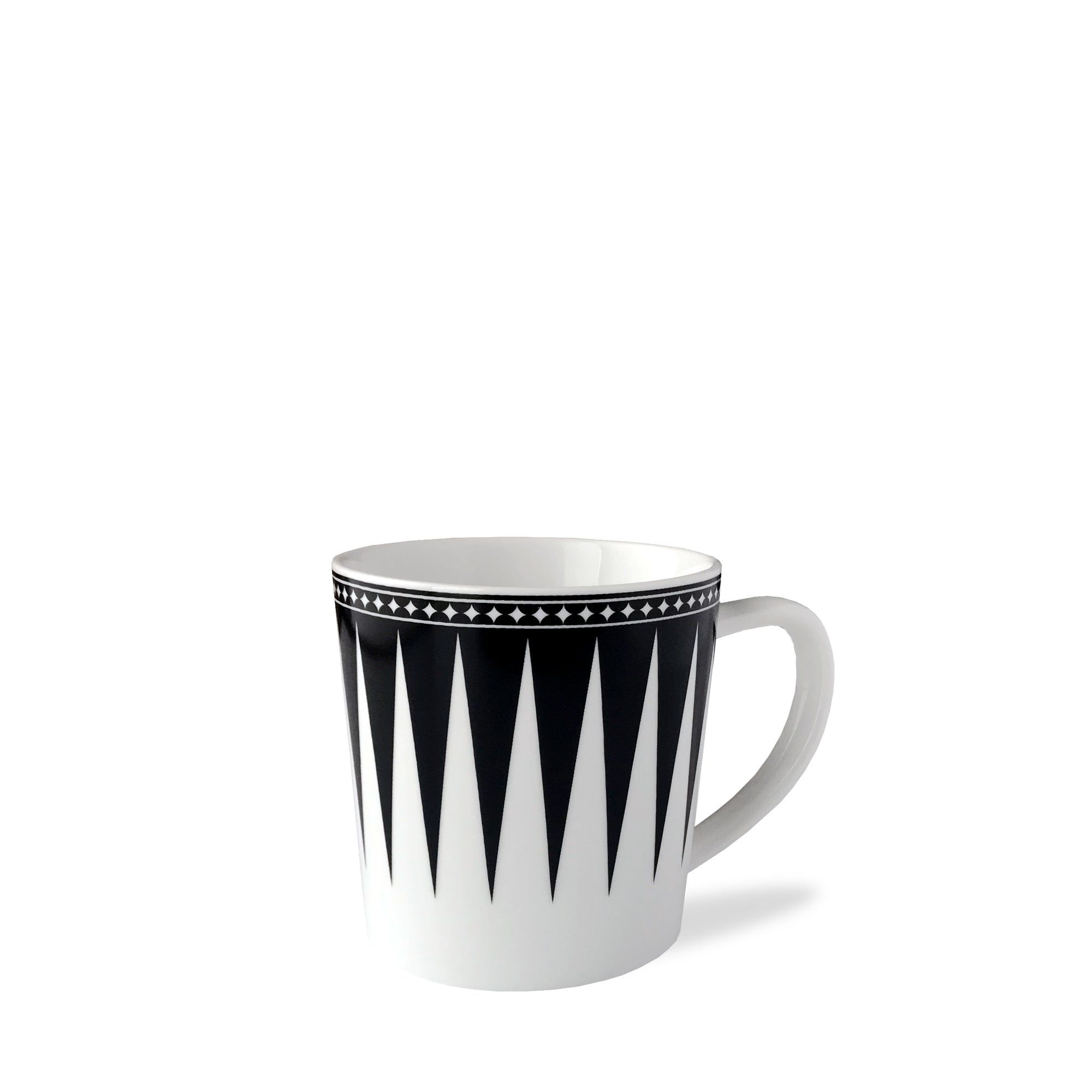 The Marrakech Mug by Caskata Artisanal Home is a white high-fired porcelain coffee mug with a black geometric triangular pattern and a black border adorned with small white stars near the rim, reminiscent of Art Deco designs.
