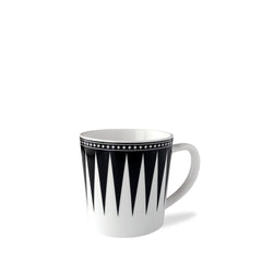 The Marrakech Mug by Caskata Artisanal Home is a white high-fired porcelain coffee mug with a black geometric triangular pattern and a black border adorned with small white stars near the rim, reminiscent of Art Deco designs.