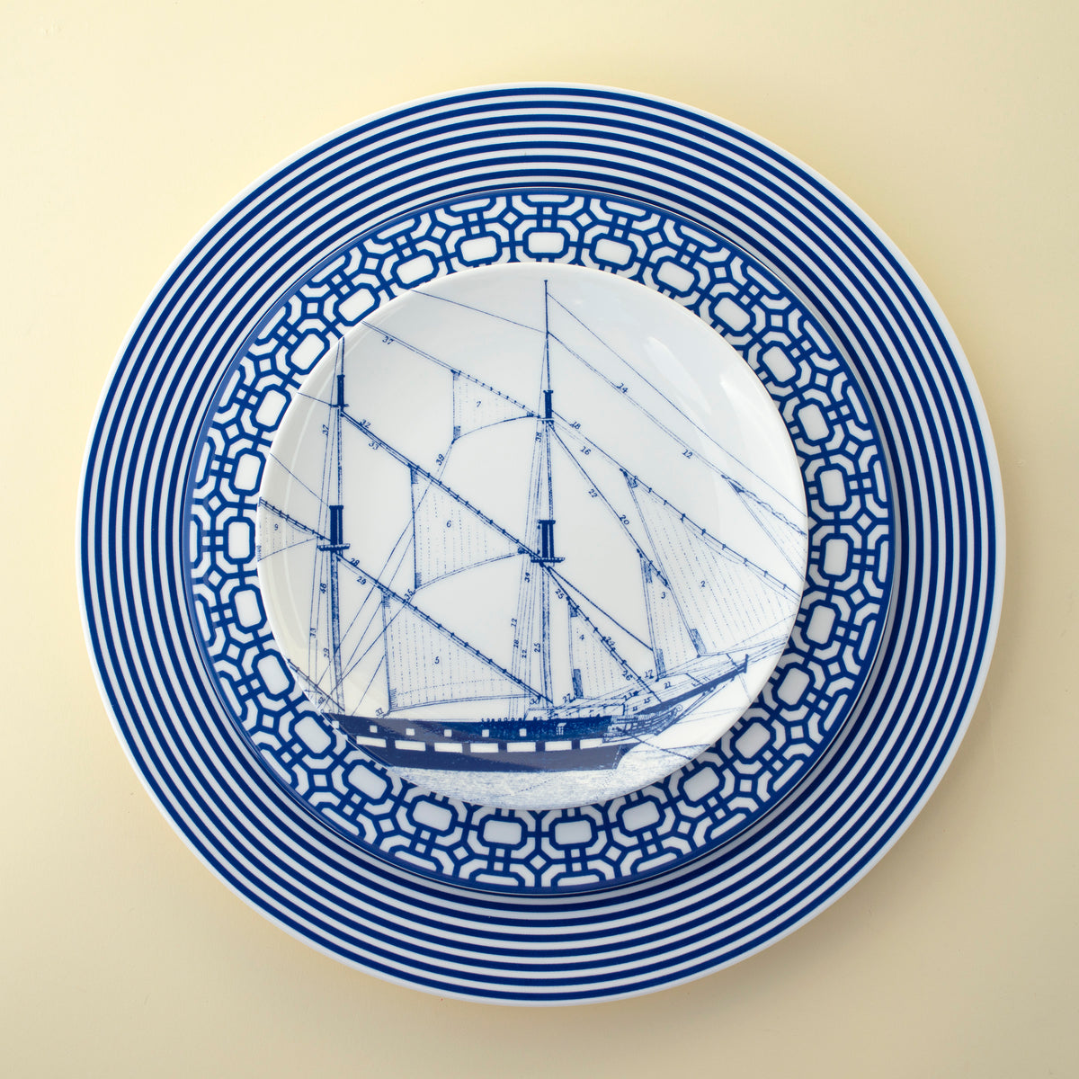 A Caskata Artisanal Home Rigging Small Plate with a blue and white pattern featuring a ship illustration in the center is pictured against a plain background, embodying vintage illustrations that celebrate nautical heritage.