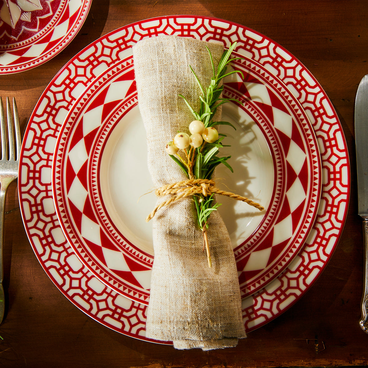 A place setting of premium porcelain Newport Garden Gate Crimson Dinner and Fez Crimson Salad plates by Caskata with a natural linen napkin tied with a rosemary sprig and berries.